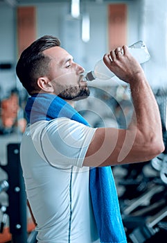 Young adult man drinking bottle of water on trreadmill in gym.