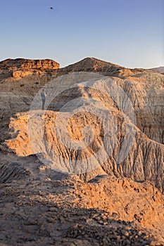 Young adult man flying drone in semi-desert area with erosional figures and cliff