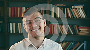 Young adult man with glasses smiling and looking at camera. Student in library