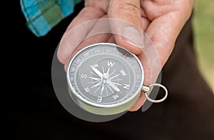 Young adult man holding a simple compass in hand outdoors, object detail, extreme closeup. Finding the right direction, seeking,