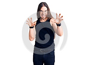 Young adult man with long hair wearing goth style with black clothes smiling funny doing claw gesture as cat, aggressive and sexy