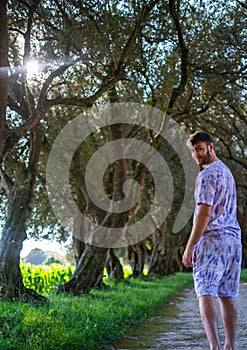 Young adult man in the park looks at the camera. Handsome guy posing outdoors on green palms background.