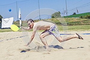 Young adult man plays tennis on the beach