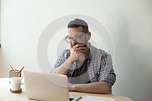 Young adult man reading awful news article in his laptop compute