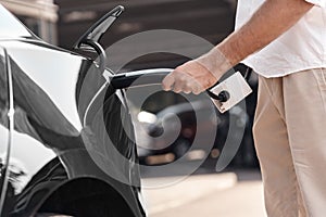 Young adult man standing near electric car, charging battery