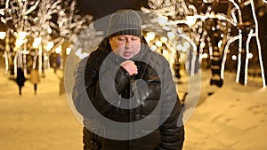 A young adult man in winter city street. He freezes, rubs his hands and shivers from the cold