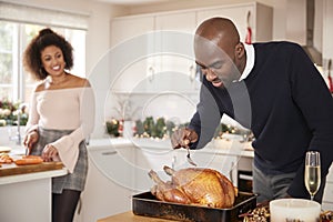 Young adult mixed race couple preparing Christmas dinner together at home, man basting roast turkey in the foreground, front view,