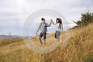 Young adult mixed race couple walking down a hill hand in hand during a mountain hike