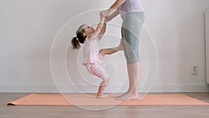 Young adult mother doing exercises with little baby girl at home
