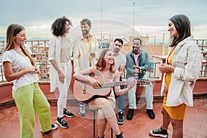 Young adult musician woman playing a guitar and singing a song to her best friends, enjoying a rooftop party with her