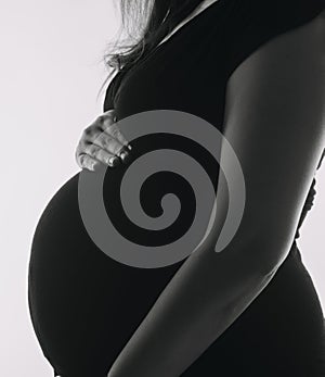 Young adult pregnant woman in white clothes touching big naked belly with hands. Showing shape. Pregnancy concept. Expectation