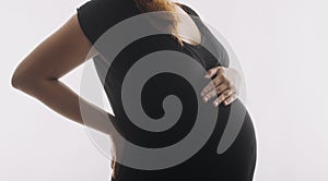 Young adult pregnant woman in white clothes touching big naked belly with hands. Showing shape. Pregnancy concept. Expectation