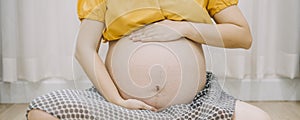 Young adult pregnant woman in white clothes touching big naked belly with hands. Showing shape. Pregnancy concept. Expectation