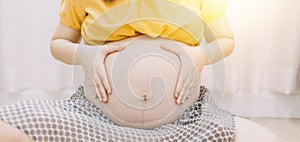 Young adult pregnant woman in white clothes touching big naked belly with hands. Showing shape. Pregnancy concept. Expectation