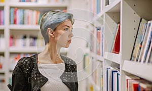 Young adult punk girl in library lookin on books