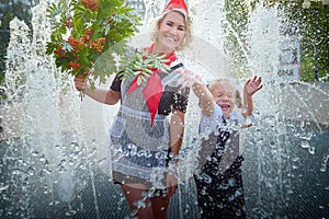 Young and adult schoolgirl on September with flowers having fun near water of fontain. Generations of schoolchildren