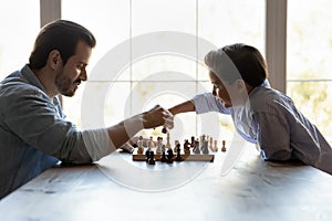 Young adult single dad playing chess with preteen son