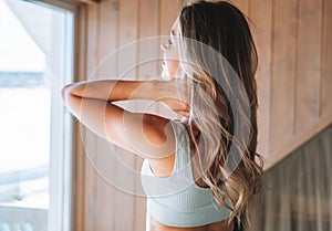 Young adult slim fitness blonde woman does morning exercises near the window of home