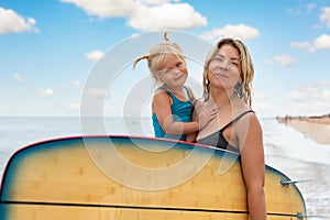 Young adult slim sporty female surfer girl enjoy having fun swimming together with cute little baby girl surfboard ocean