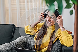 Young adult smiling cheerful girl woman listening to music from smartphone wearing wireless headset headphones while lying down on