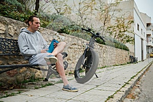 Young adult sportsman, athletic man cyclist relaxing when riding electric bike in the city, holding a bottle of water
