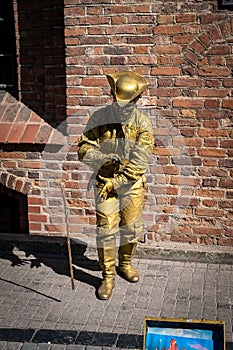 Young adult street performer dressed in a gold outfit standing still