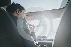 Young adult using smart phone on a sunny day inside a modern car