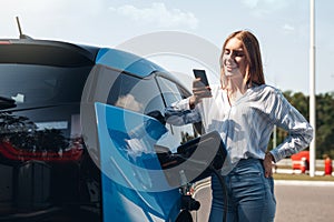 Young adult using smartphone and charging electric car