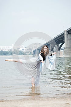 Young adult white female woman on a beach doing arabesque in the water