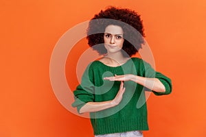Young adult woman with Afro hairstyle wearing green casual style sweater showing time out hand