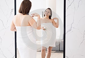 Young adult woman apply body cream look in mirror