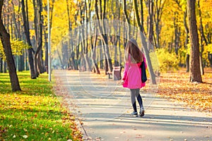 Young adult woman in bright casual coat walking along beautiful golden colored autumn park alley. Happy attractive sporty girl in