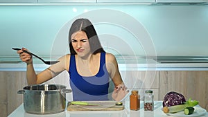 Young adult woman cooking soup and tasting it