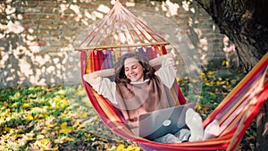 A young adult woman freelancer relaxing lying on a hammock with a laptop