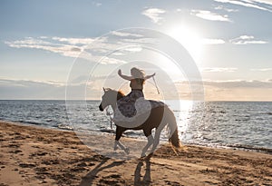 Young adult woman happily riding a horse on a beach on a sunny day