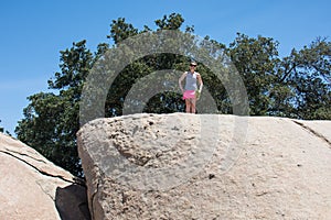 Young adult woman hiker stands on top of a giant boulder rock in San Diego California