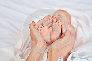 Young adult woman holding little new born baby feet in hands