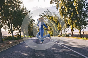 Young adult woman jumping happy in the middle of long straight asphalt road. Concept of travel people and freedom happiness