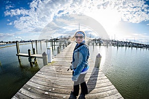 Young adult woman with long blonde hair whips her hair as she turns around on a seaside dock in Maryland photo