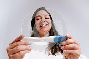 Young adult woman looking at pregnancy test with happy expression in her bedroom. latino woman with dark hair in her thirties