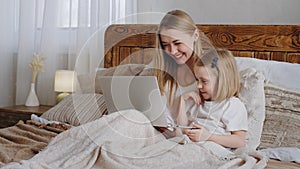 Young adult woman mom Caucasian mother hugs cuddles little daughter child baby look together in laptop screen choose