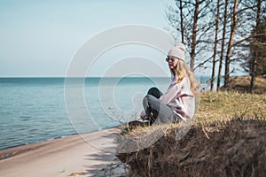 Young adult woman in pink hat sitting alone on the bluffs, looking of sea, freedom concept, peaceful atmosphere