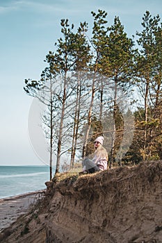 Young adult woman in pink hat sitting alone on the bluffs, looking of sea, freedom concept, peaceful atmosphere