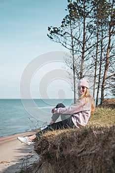 Young adult woman in pink hat sitting alone on the bluffs, looking of sea, freedom concept, peaceful atmosphere
