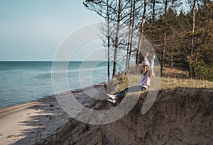 Young adult woman in pink hat sitting alone on the bluffs, looking of sea, freedom concept, peaceful atmosphere