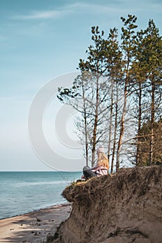 Young adult woman in pink hat sitting alone on the bluffs, looking of sea, freedom concept, peaceful atmosphere