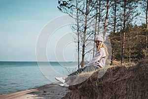 Young adult woman in pink hat sitting alone on the bluffs, looking of sea, freedom concept, peaceful atmosphere