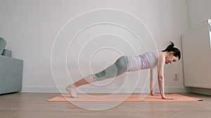 Young adult woman practising yoga on a mat at home