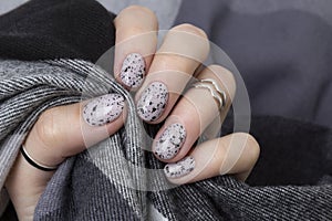 Young adult woman`s hands with pink nude fashionable nails on gray concrete background