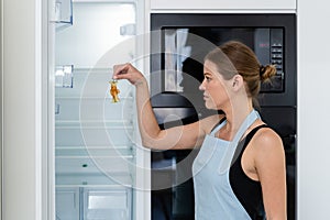 Young adult woman standing near refrigerator with apple